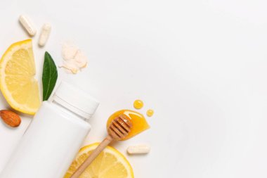 Limon dilimleri, haplar ve gri arka planda bal içeren boş plastik vitamin şişesi