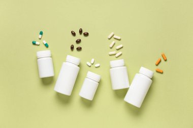 Boş plastik vitamin şişeleri ve yeşil arka planda farklı haplar.