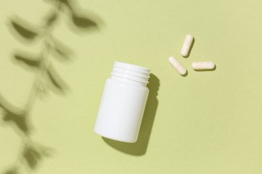 Yeşil arka planda hapları olan boş plastik vitamin şişesi.