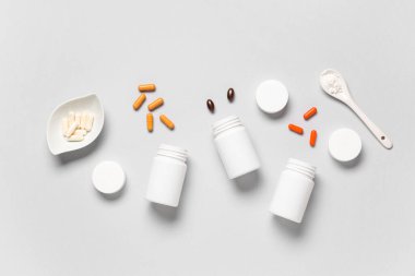 Farklı haplarla dolu boş plastik vitamin şişeleri ve gri arka planda bir kaşık toz.