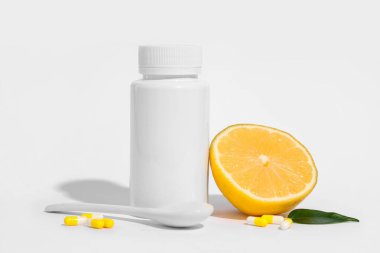 Boş plastik vitamin şişesi, içinde haplar, limon ve kaşık toz gri arka planda.