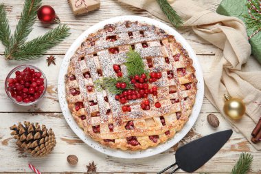 Köknar dalları ve beyaz ahşap arka planda Noel topları olan lezzetli kızılcık turtası.