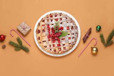 Köknar dalları, baston şekerleri ve kahverengi arka planda Noel topları olan lezzetli kızılcık turtası.