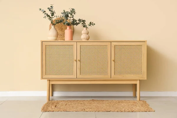 Oturma odasındaki tahta çekmecelerin üzerinde taze okaliptüs dalları olan vazolar.