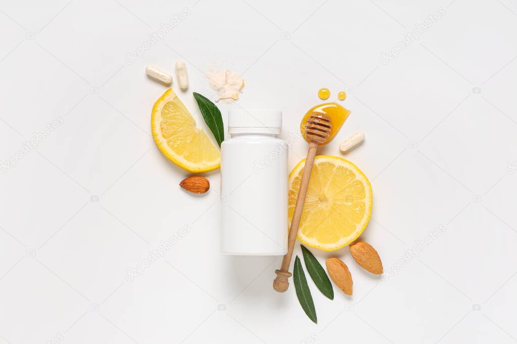 Blank plastic vitamin bottle with slices of lemon, pills, honey and almond nuts on grey background