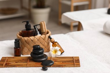Spa taşlı bambu hasırı, masaj fırçası, plumeria çiçeği ve kuafördeki kanepede duran kozmetik ürünler sepeti.