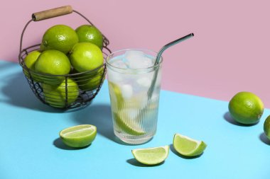Bir bardak limonlu su mavi masada pembe arka planda.