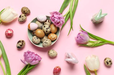 Composition with plate of Easter quail eggs, bunnies and tulip flowers on pink background