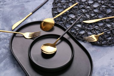 Mavi arka planda altın çatal bıçak takımı olan tabak.