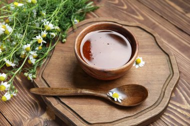 Tahta arka planda bir kase bal ve taze papatya çiçeği, yakın plan.