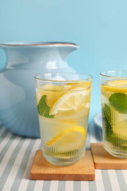 Mavi arka planda limonlu ve naneli bardaklar ve bir sürahi eritilmiş su.