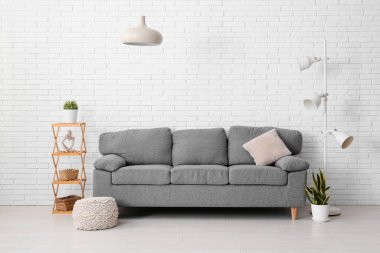 Oturma odasında yumuşak puf ve asılı lambayla şık gri kanepe.