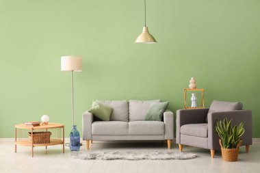 Oturma odasındaki yeşil duvarın yanında rahat koltuğu ve lambaları olan şık gri kanepe.