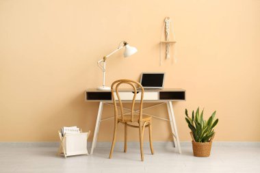 Modern dizüstü bilgisayar ve lamba ofis odasındaki bej duvarın yanındaki masada.