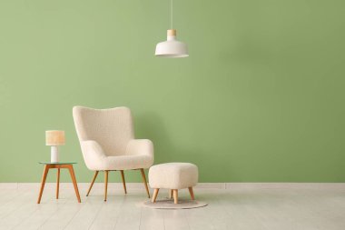 Oturma odasındaki yeşil duvarın yanında yumuşak puf ve modern lambalı şık bir koltuk.