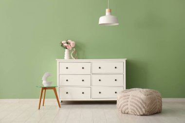 Çekmece dolabında güzel çiçekler ve modern odada yeşil duvarın yanında asılı bir lamba olan bir vazo.