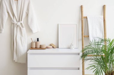 Banyodaki beyaz duvarın yanında fotoğraf çerçevesi ve banyo malzemeleri olan çekmeceler.