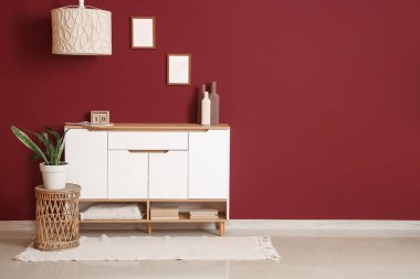 Oturma odasının iç tarafındaki kırmızı duvarın yanındaki çekmeceler, masa ve bitkiler.