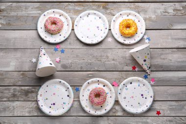 Gri ahşap zemin üzerinde parti şapkaları ve çörekleri olan tek kullanımlık kağıt tabaklardan yapılmış çerçeve.