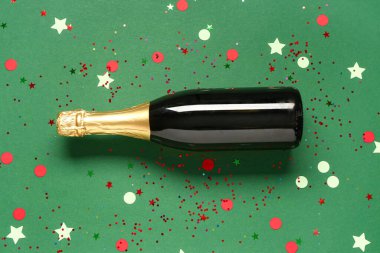 Yeşil arka planda konfeti olan şampanya şişesi.