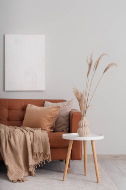 Rahat bir kanepe ve kahve masası. Oturma odasının içindeki vazoda otlar var.