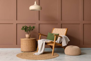 Yumuşak puflu şık koltuk ve kahverengi duvarın yanındaki hasır masa.