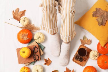 Sonbahar yaprakları, kitaplar, bir fincan kahve ve yatağın üzerinde balkabağı olan kadın çorapları.