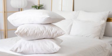 Beyaz battaniyeli rahat yatak ve şık yatak odasında yumuşak yastıklar, yakın çekim.