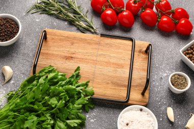 Ahşap mutfak tahtası, taze otlar, domatesler ve arkaplanda baharatlar.