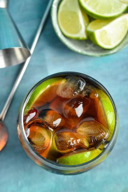 Bir bardak soğuk Küba kokteyli ve mavi arka planda limonlu kase.