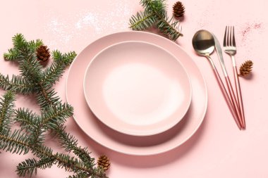 Noel sofrasında köknar ağacı dalları, kozalaklar, tabaklar ve pembe arka planda çatal bıçak seti