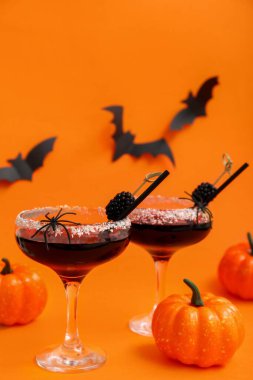 Cadılar Bayramı için turuncu arka planda böğürtlen ve balkabağı olan lezzetli kokteyller.