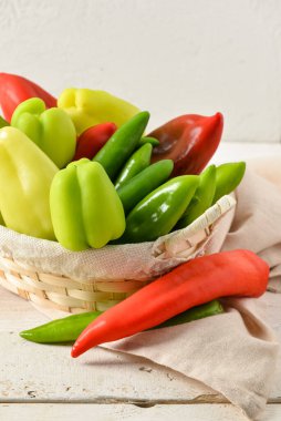 Beyaz ahşap masada farklı taze biberli hasır sepet.