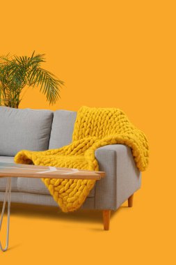 Modern oturma odası içi gri kanepe, örgü battaniye ve sarı arka planda masa.