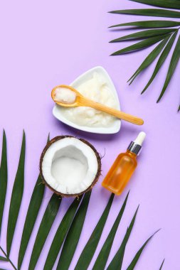 Bir kase hindistan cevizi kozmetik yağı ve leylak arkaplanda palmiye yaprakları.