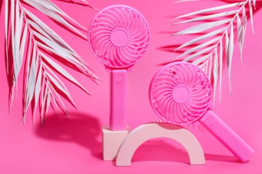 Taşınabilir elektrikli fanlar ve pembe arka planda palmiye yapraklarıyla sıva podyumu, yakın plan.