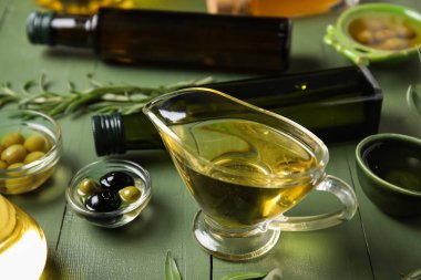 Yeşil ahşap arka planda taze zeytin yağıyla sos kabı ve kaseler.