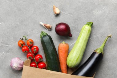Gri arka planda içi taze sebzelerle dolu kağıt torba.