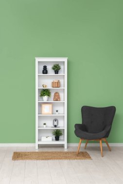 Yeşil duvarın yanında siyah koltuğu ve halısı olan modern raf ünitesi