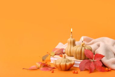 Turuncu arka planda balkabağı, kitap ve sonbahar yaprakları şeklinde yanan mumlarla güzel bir kompozisyon.
