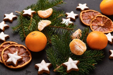 Yıldız şeklinde mandalinli zencefilli kurabiye, kurutulmuş portakal ve siyah arkaplanda köknar dalları