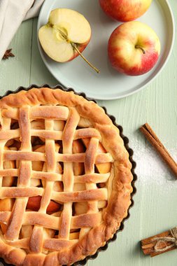 Lezzetli ev yapımı elmalı turta, yeşil ahşap arka planda meyve ve tarçın.