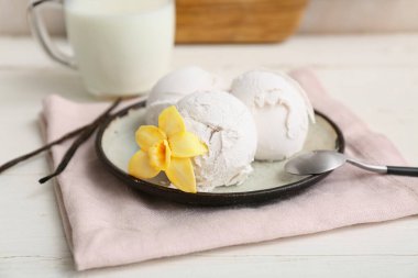 Çiçekli ve beyaz ahşap masaya saplanmış vanilyalı dondurma topları.