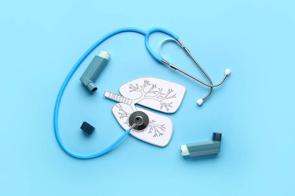Composition with inhalers, paper lungs and stethoscope on blue background