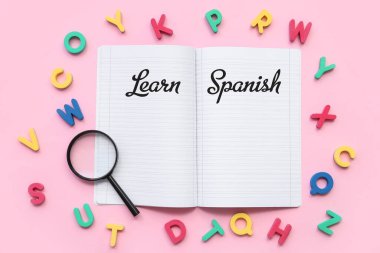 Pembe zemin üzerinde boş defter, büyüteç ve renkli harflerle kompozisyon