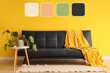 Sarı duvarın yanındaki masada ekose ve çiçekli siyah deri kanepe. Farklı renk desenleri