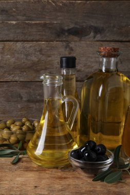 Ahşap zemin üzerinde taze zeytin yağı bulunan farklı cam eşyalar.