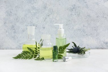 Bir şişe yağ, numune ve doğal kozmetik malzemeleriyle dolu laboratuvar bardakları grunge duvarının yanındaki beyaz masada.
