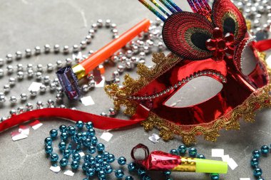 Gri arka planda parti boynuzları, konfeti ve dekoru olan güzel kırmızı karnaval maskesi. Yakın çekim.