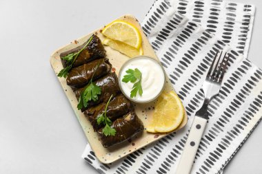 Lezzetli Dolmas tabağı (doldurulmuş üzüm yaprakları), ekşi krema, limon dilimleri ve gri arka planda peçete